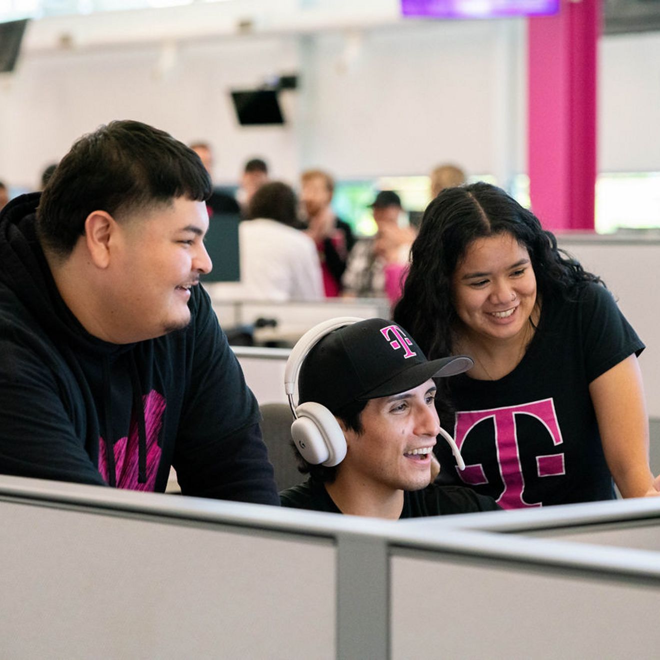 A group of T-Mobile employees is smiling as they look at a computer screen at the office.