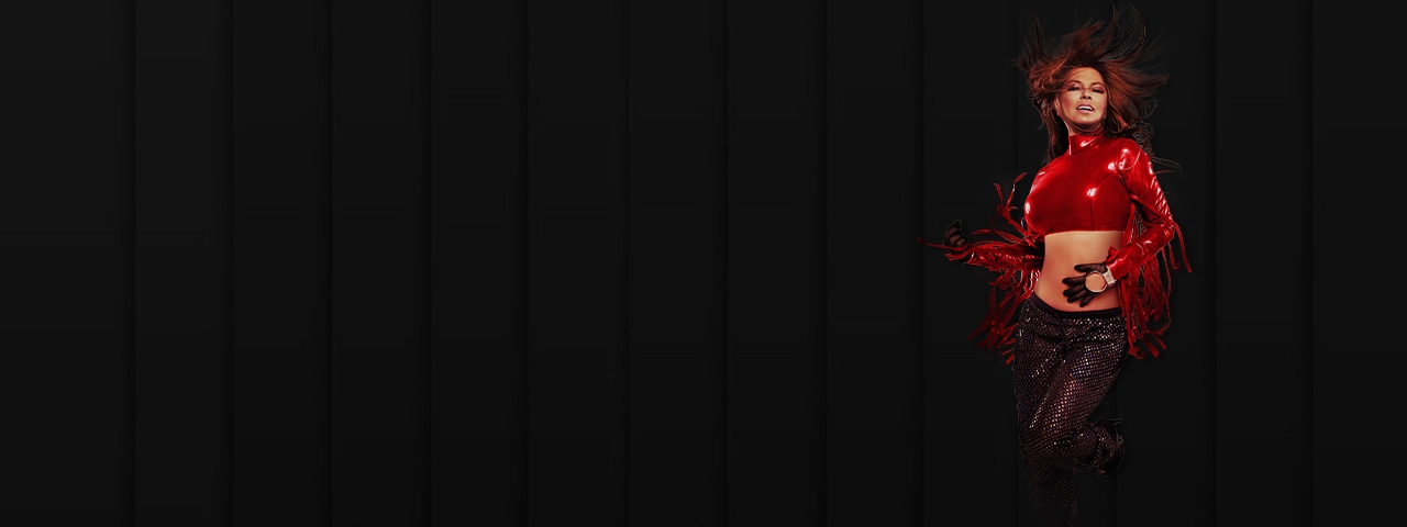 Shania Twain posing in front of a black stage curtain.