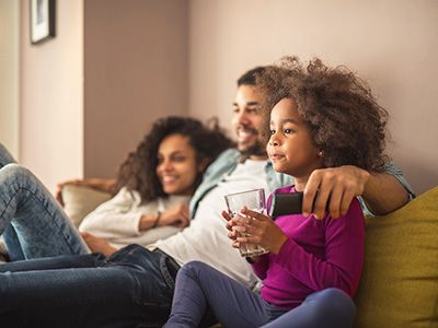 Una familia sonriendo mientras mira televisión en el sofá.