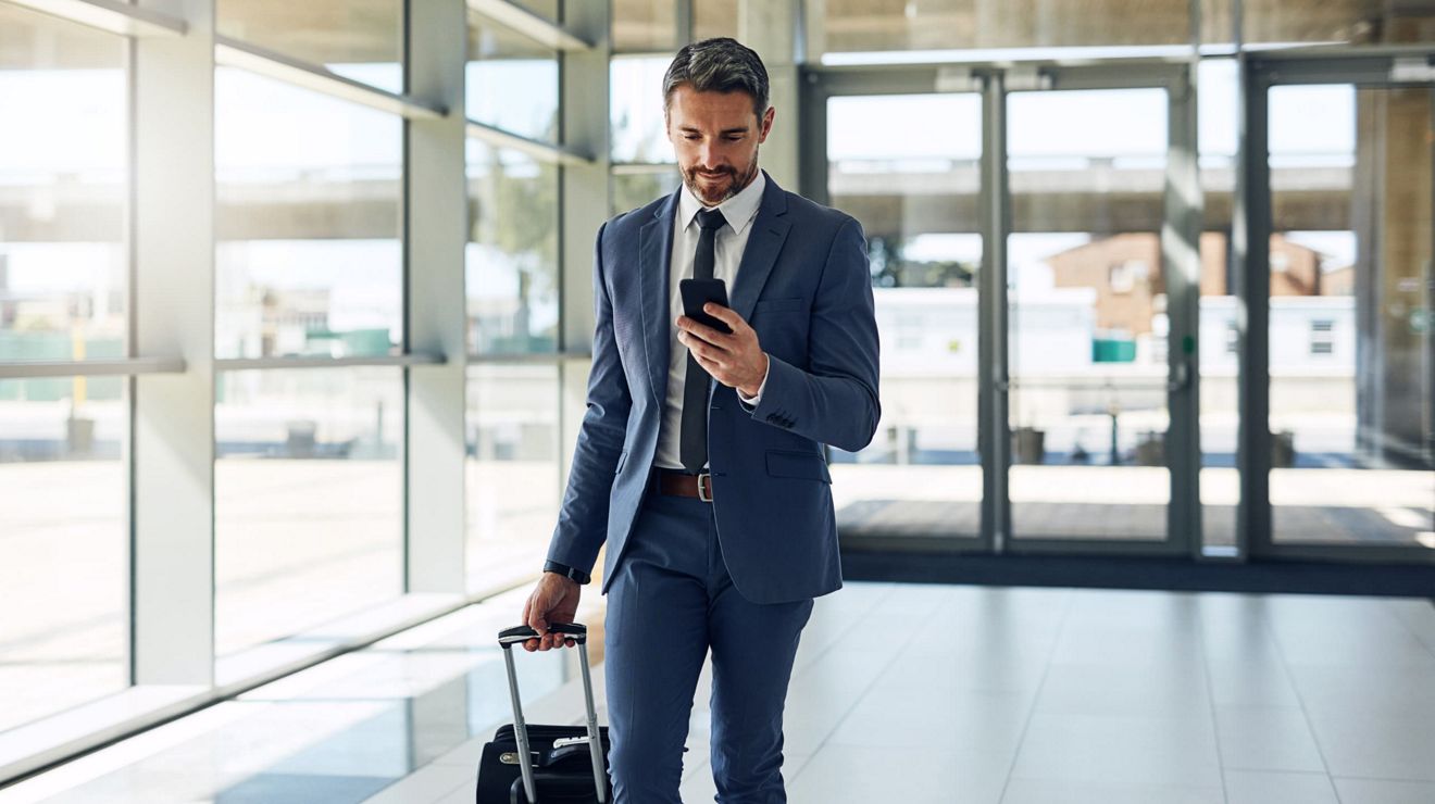  A businessperson dressed in a suit checks their mobile phone while walking in an airport.