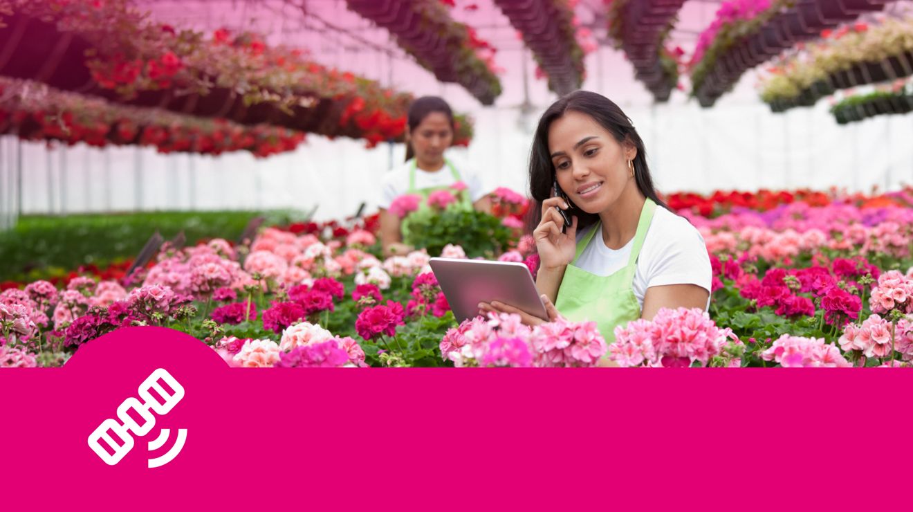 An employee at a flower nursery helps a customer on her smart phone and checks an order on a tablet.
