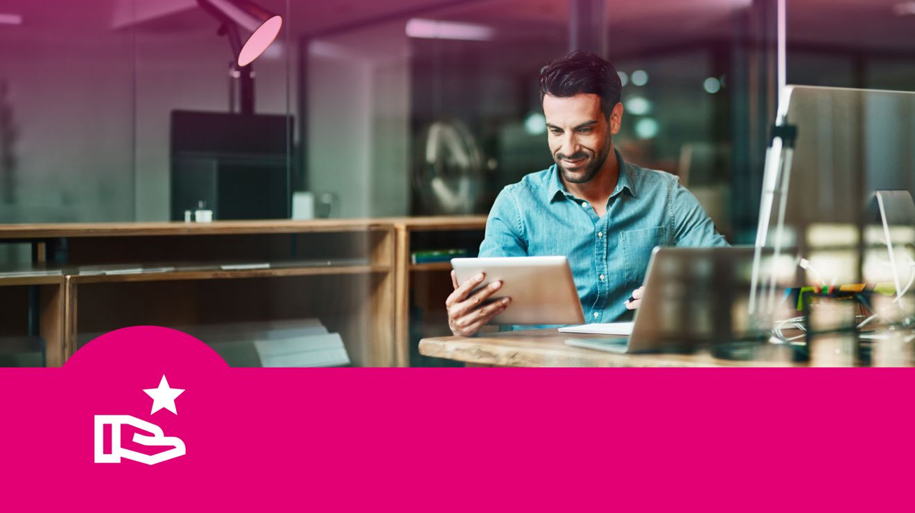A business professional at their desk gets work done on a connected tablet and a laptop computer.