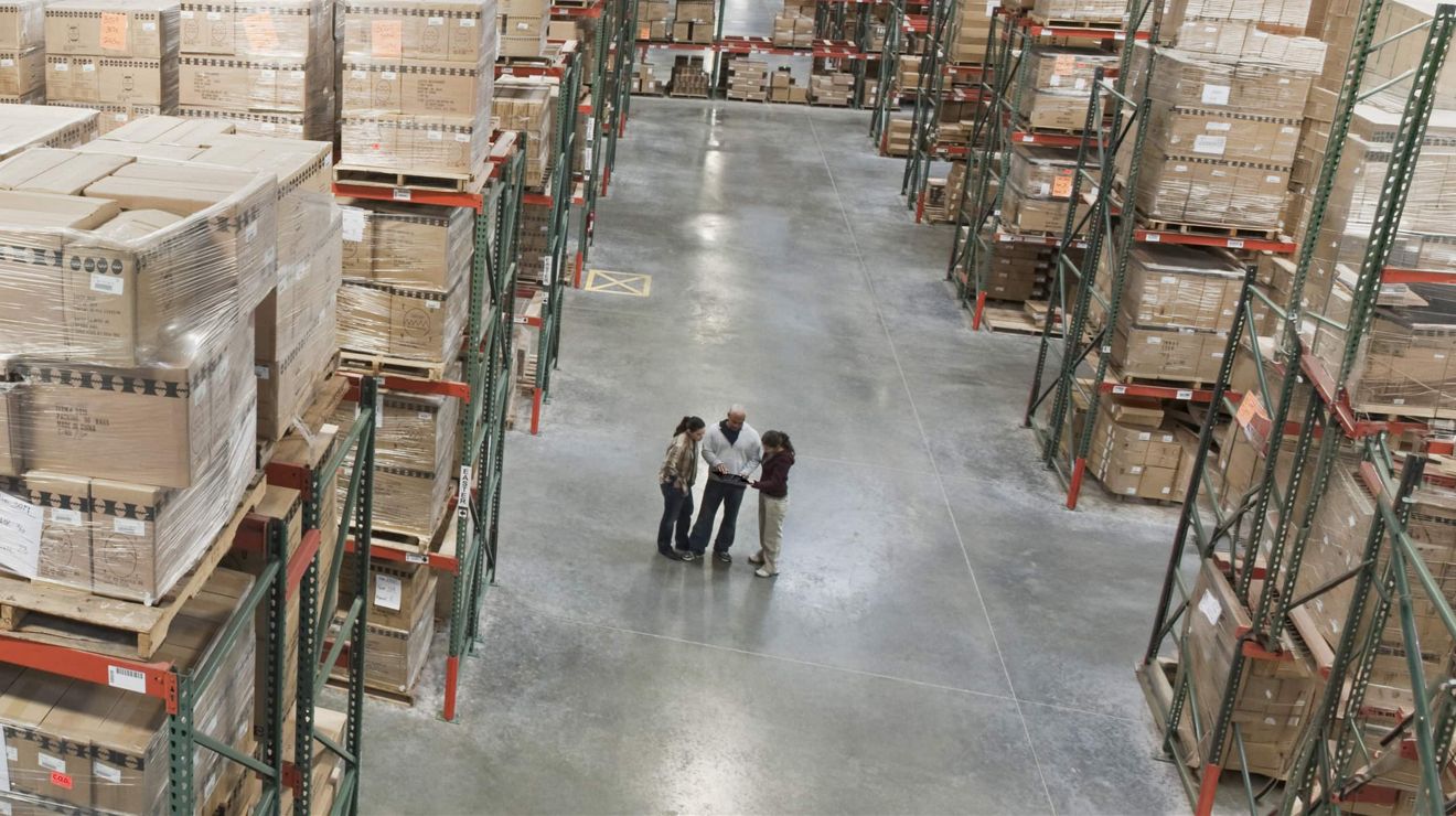 Three managers review statistics on a T-Mobile connected tablet from the floor of a warehouse.