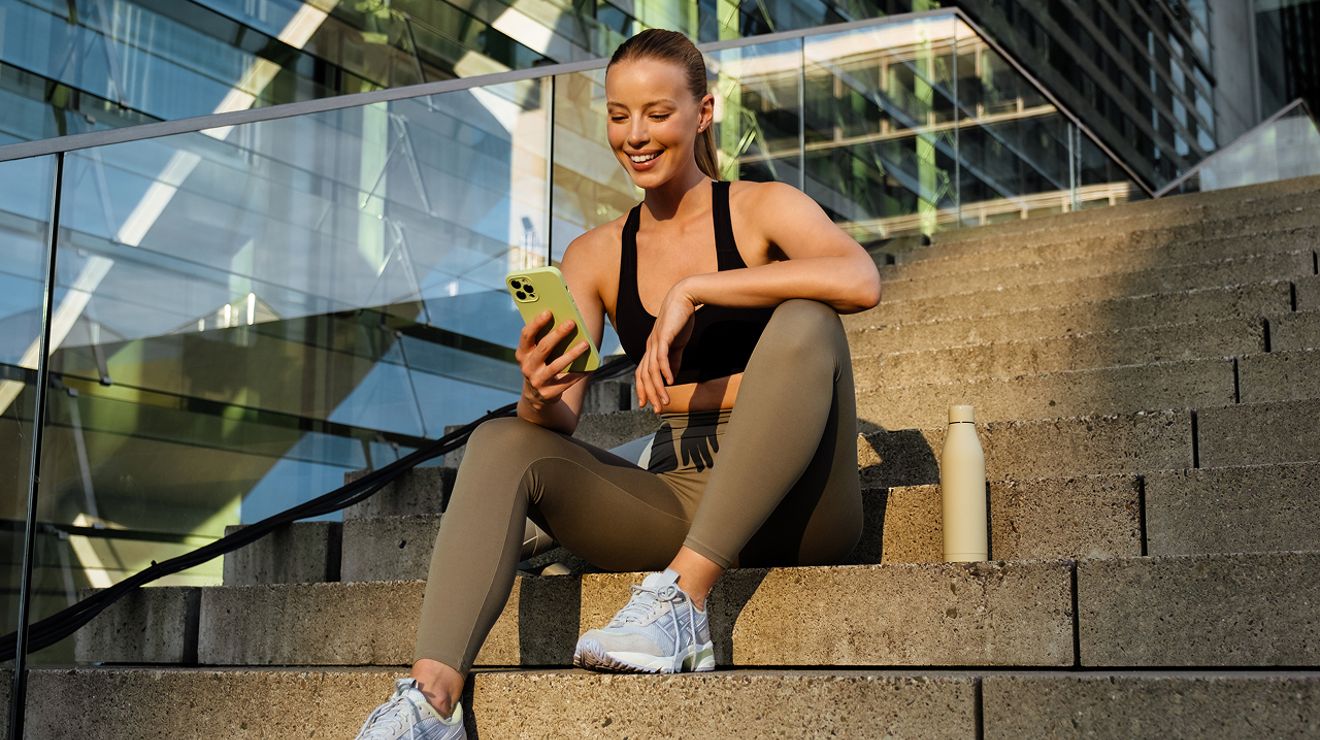 A woman smiles at her phone, dressed in gym clothes.