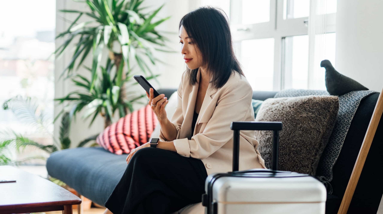 A business traveler in a sunny hotel room connects with the office on her smartphone.
