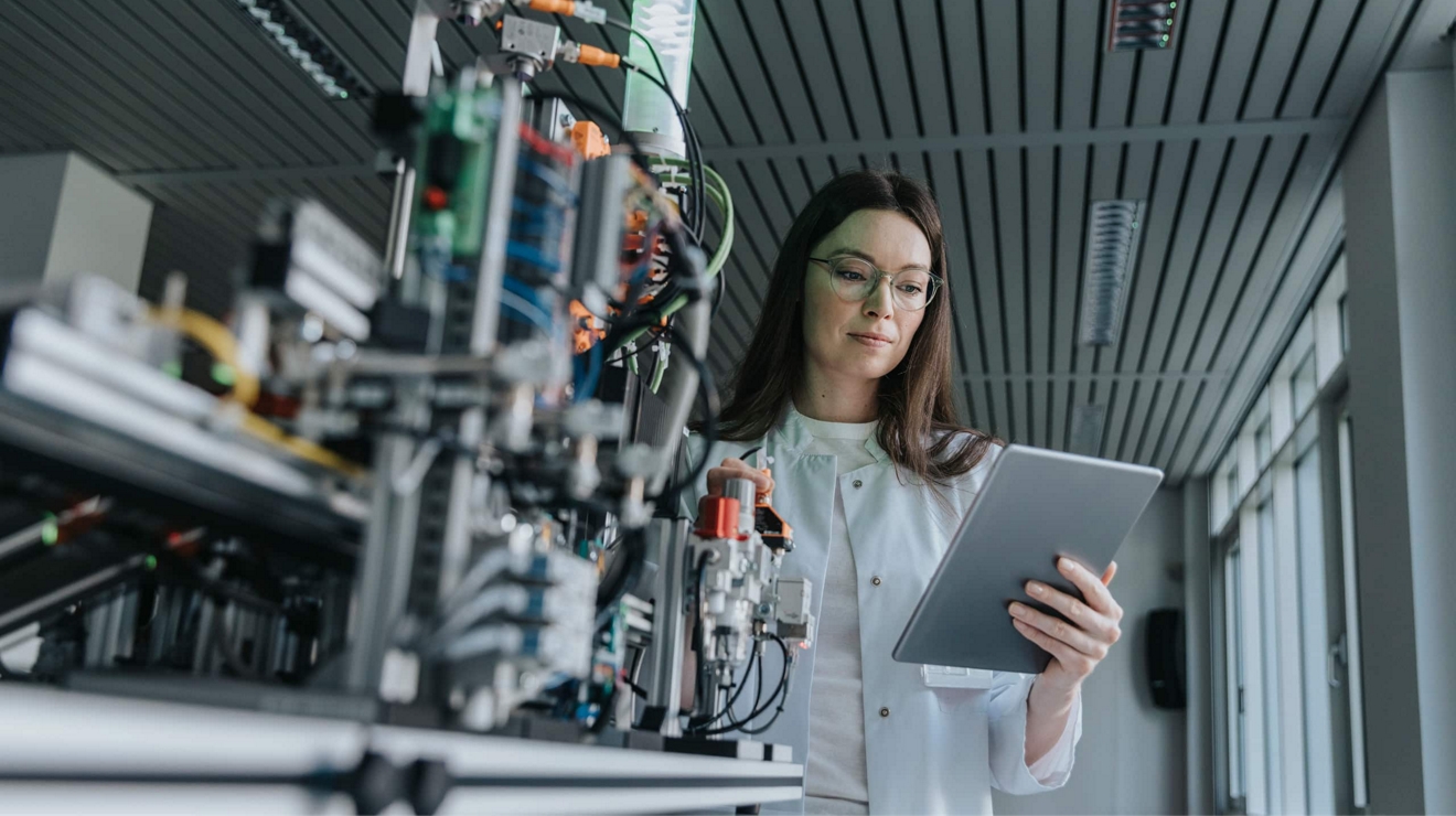 A researcher checks data on a connected laptop while working on advanced machinery.