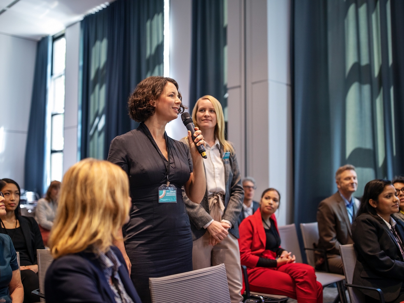 A woman is speaking to a group of people with a microphone. 