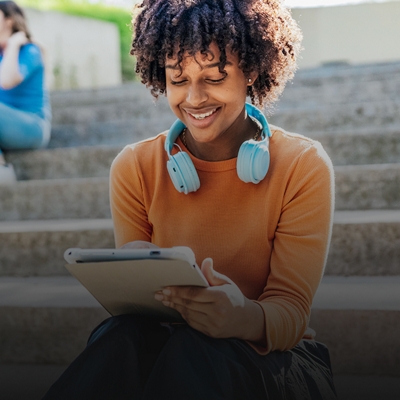 College student using a tablet while sitting on stairs outside.