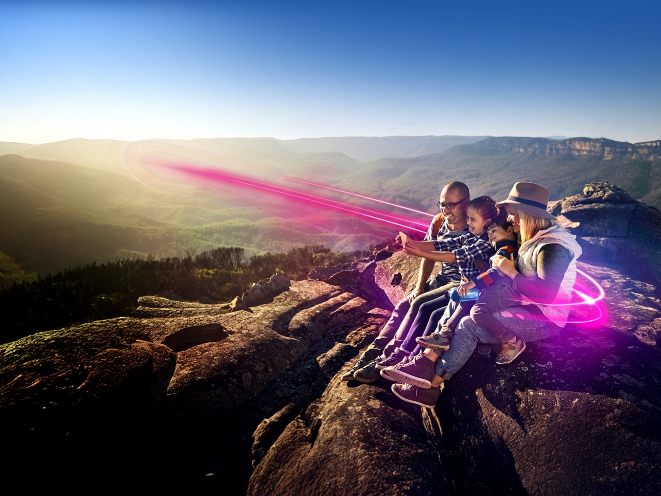 A family of four taking a selfie together on a ledge of a rock which overlooks a scenic view with a magenta aura circling above the family.