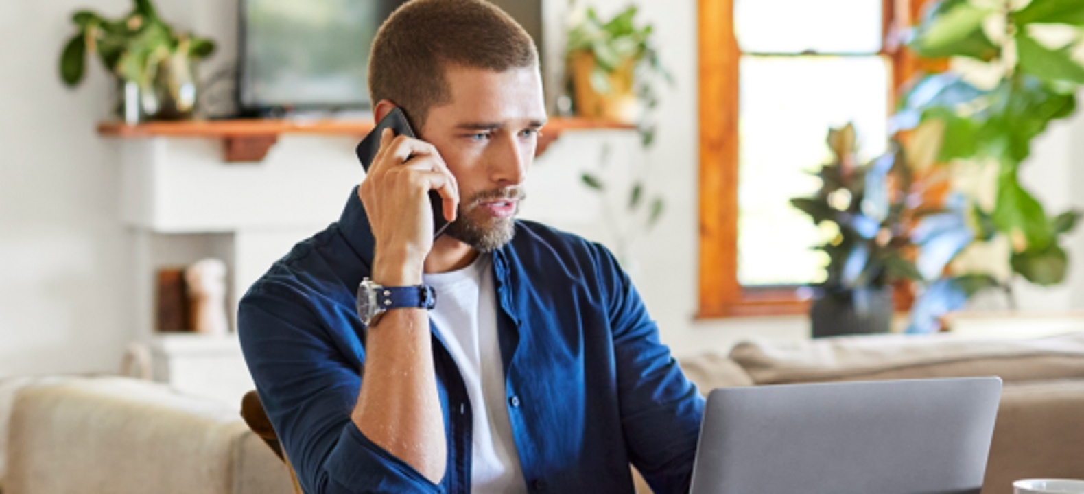 A young professional uses his smartphone and laptop while working from home.