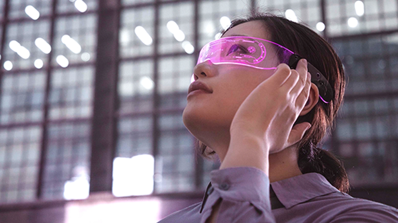 A young woman wearing augmented reality glasses gazes upwards.