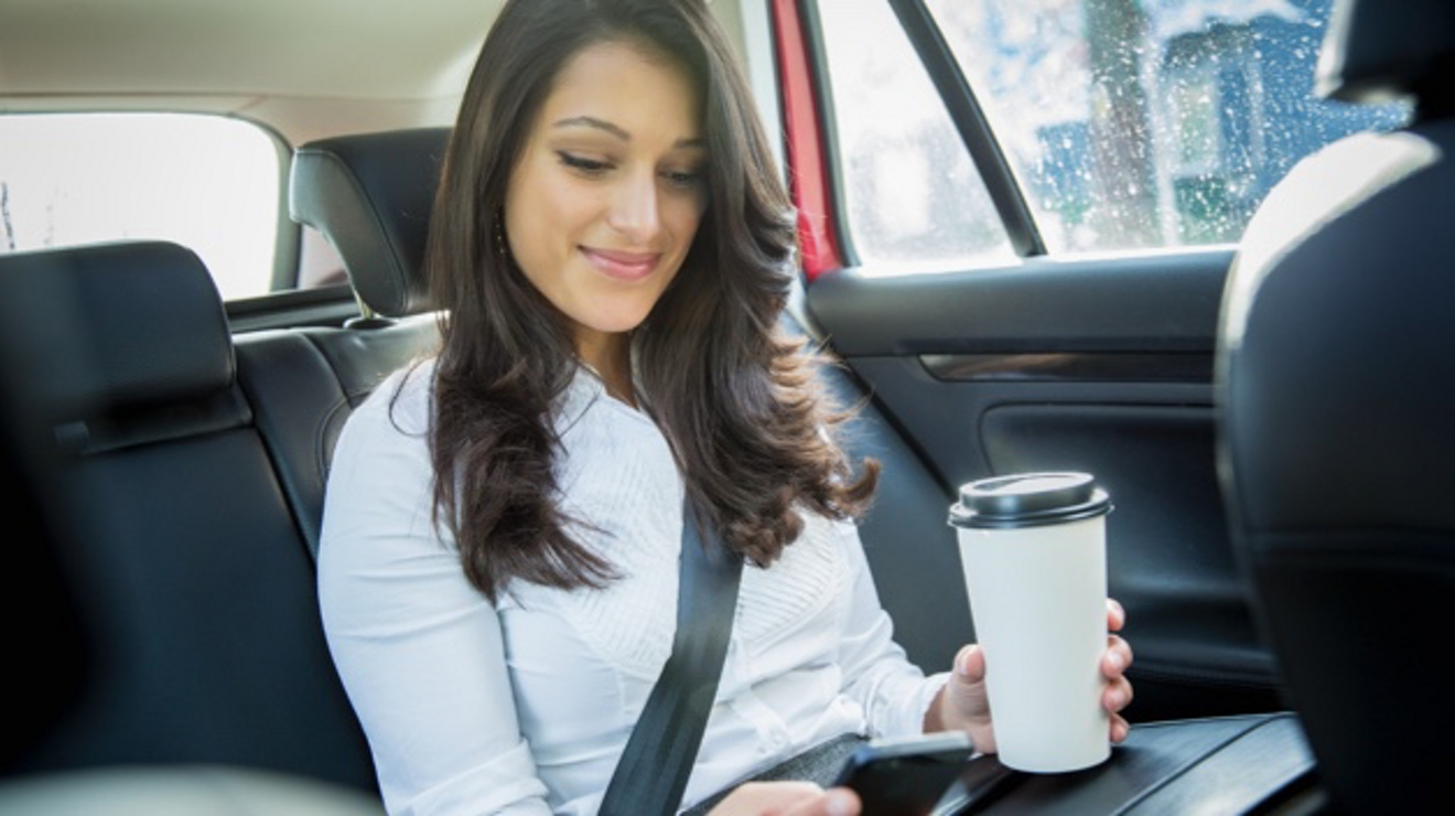 A smiling professional uses a hotspot to work on her smartphone in the backseat of a rideshare.