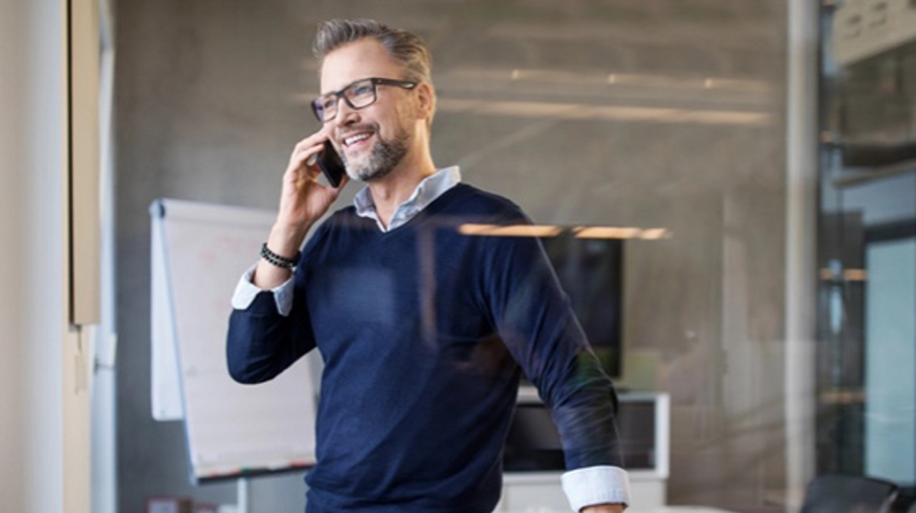 A smiling professional talks on his smartphone in a conference room.