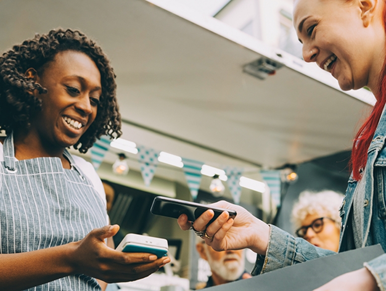 Store worker in apron uses mobile device to let customer pay with her smartphone