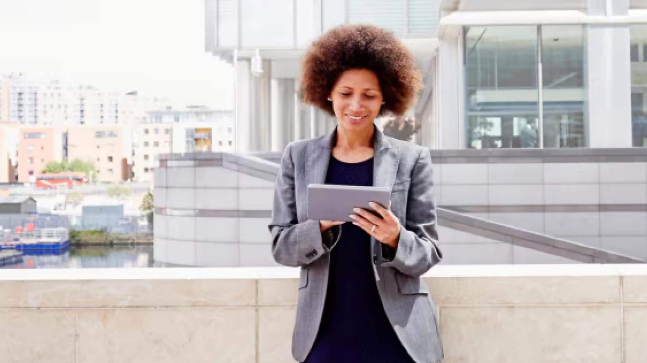 A young professional uses a tablet on an outdoor landing of her office building.