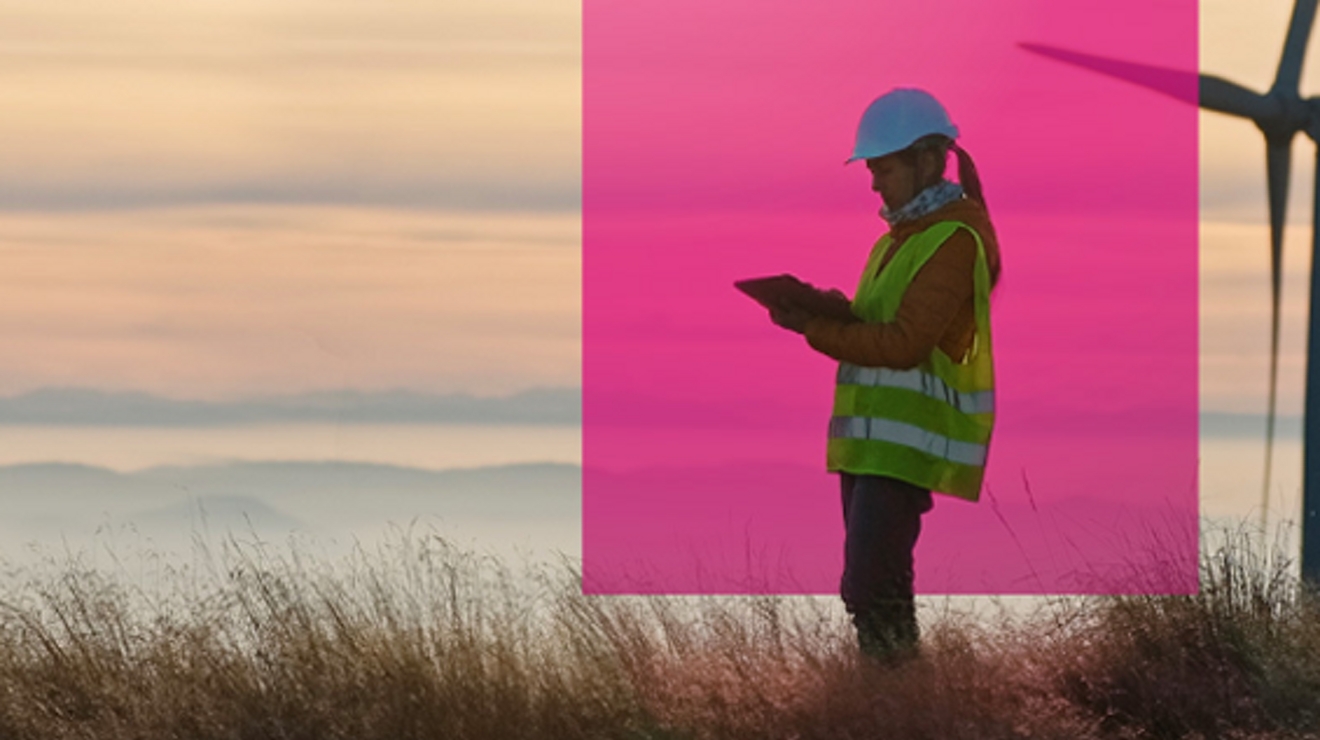 A wind energy engineer checks her tablet on a wind farm at dawn.