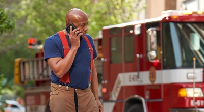 A firefighter speaks on the phone in front of a fire engine at a response site.