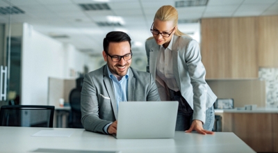 Two colleagues collaborate over a connected laptop at an office. 