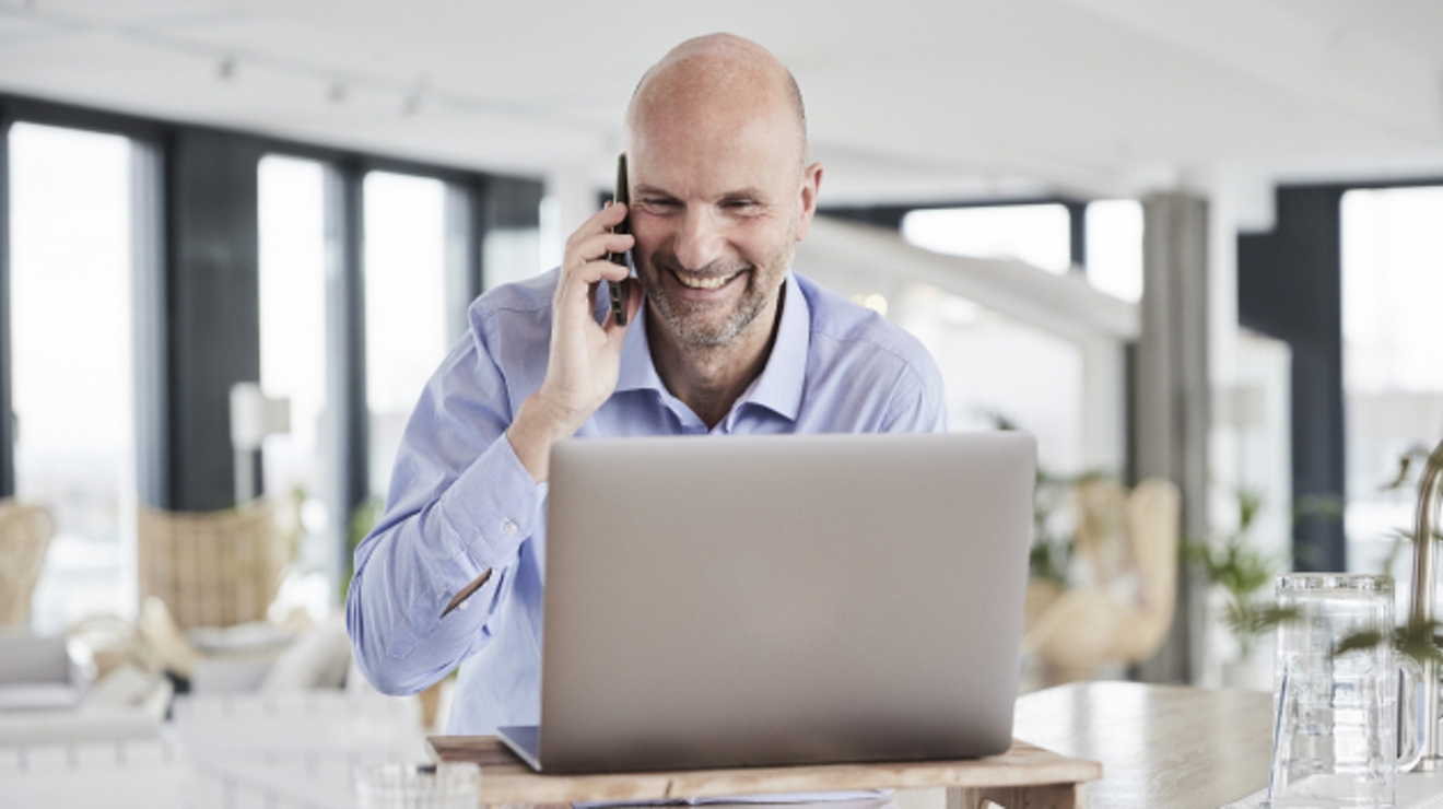 A smiling professional takes a business call while seated in front of his laptop.