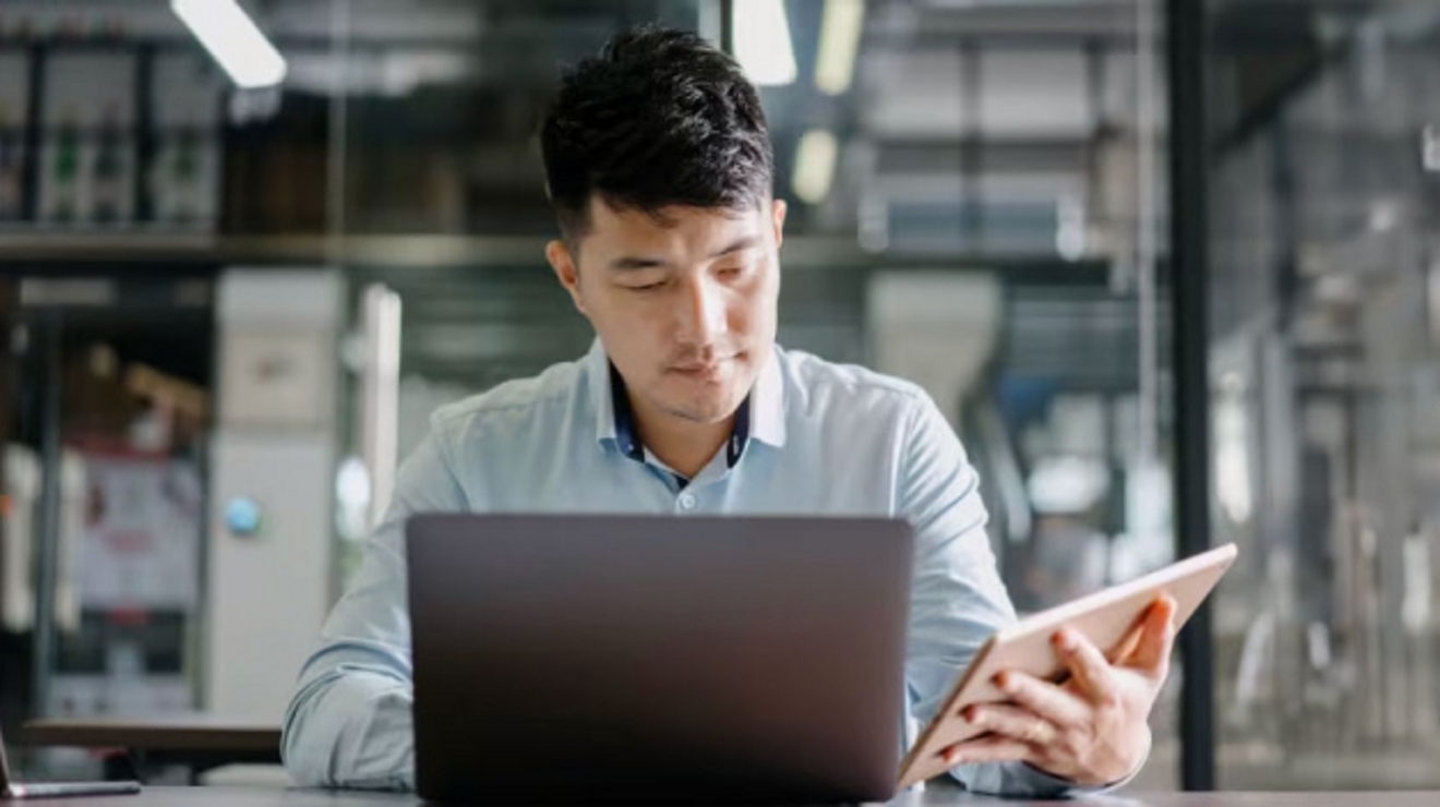 A professional works with a laptop and a tablet in an open work area.