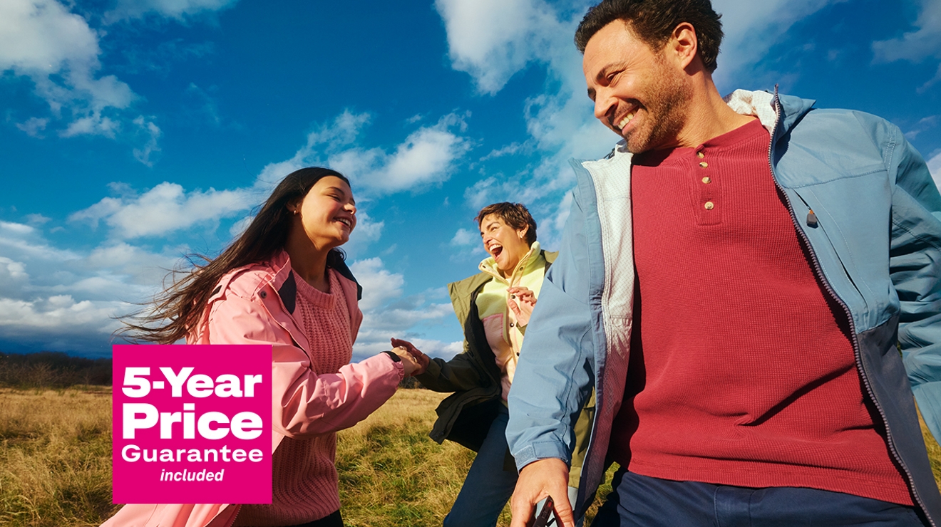 In an open field, two women and a man laugh with the words “five-year price guarantee included.”