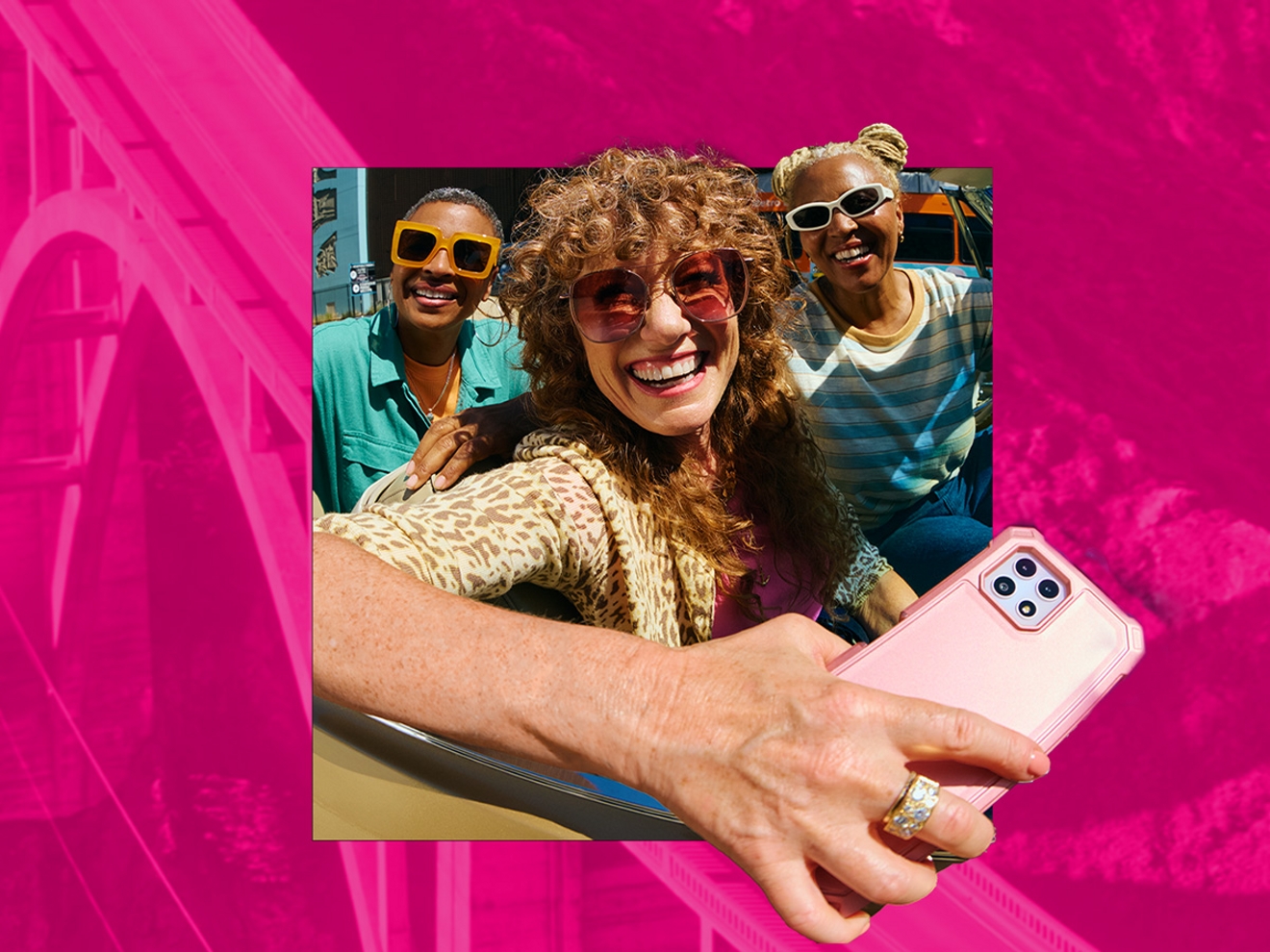 Three friends smiling in colorful sunglasses looking straight ahead as the friend in the center is holding a white smartphone featuring a pink transparent phone case.
