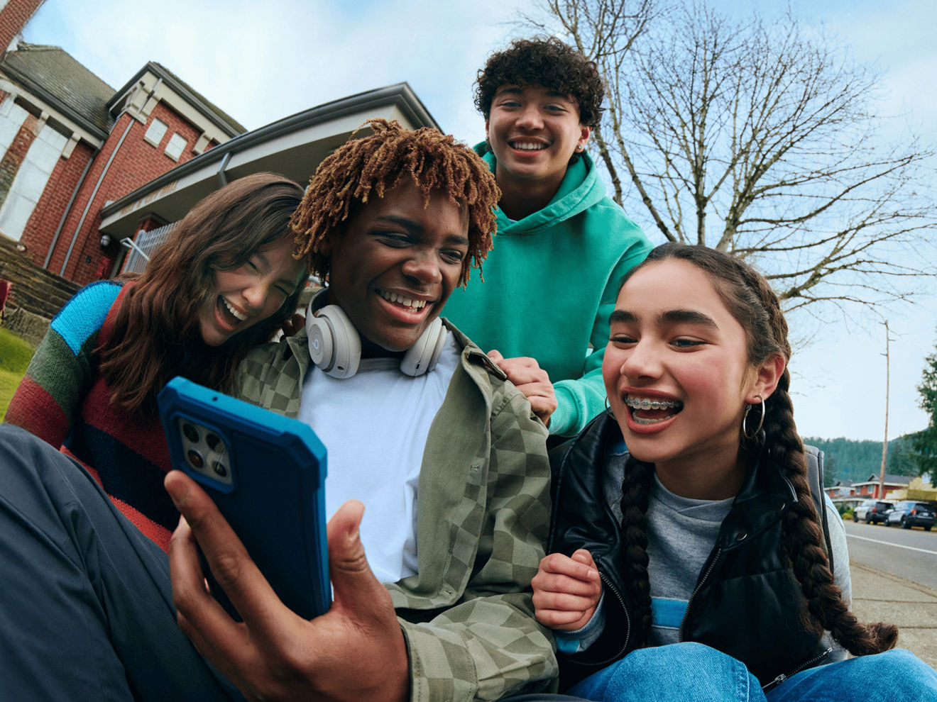 Four students huddle around a phone in front of a school.