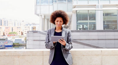 A young professional uses a tablet on an outdoor landing of her office building.