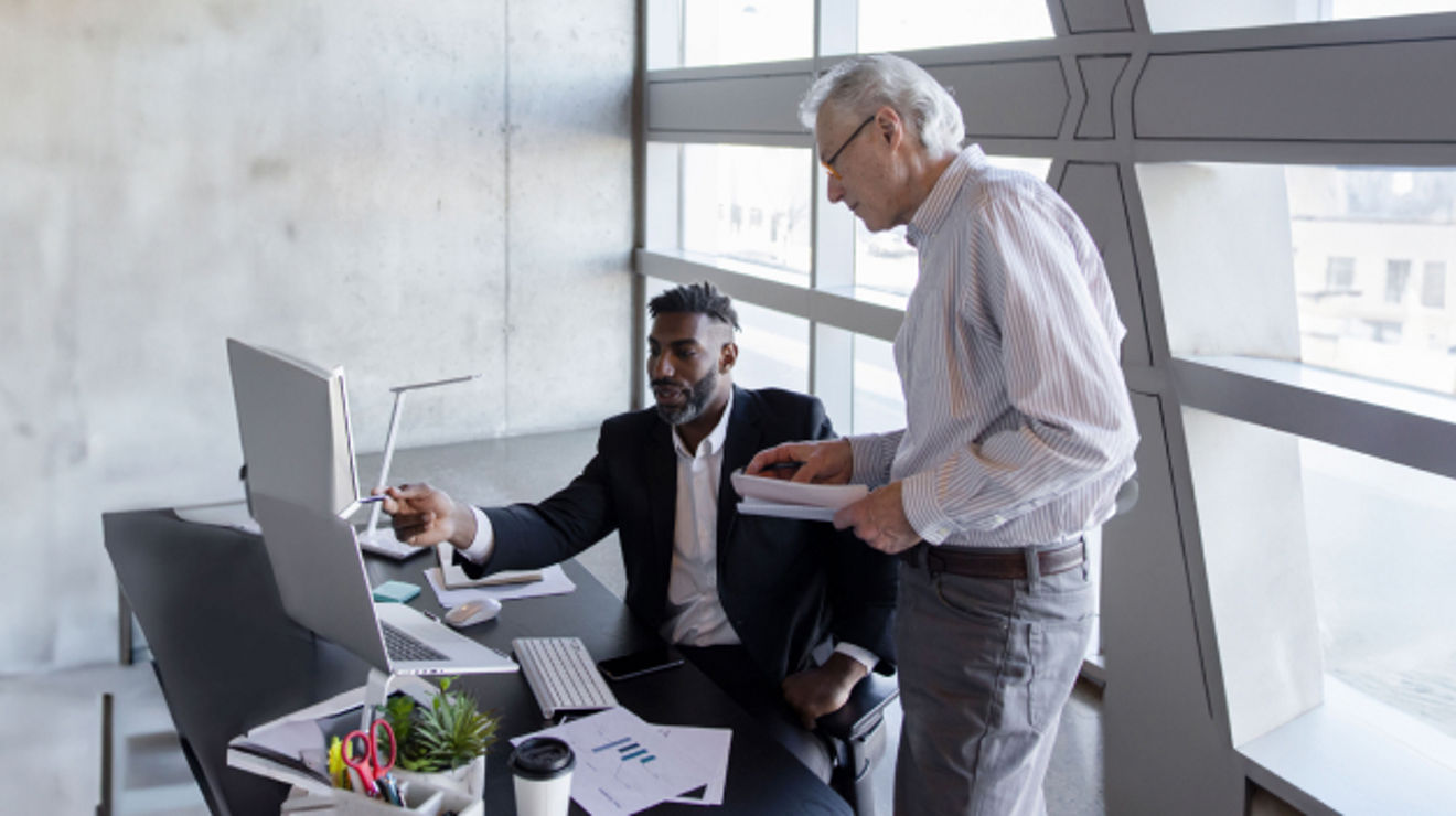 Two government employees collaborate over multiple computers at the office.