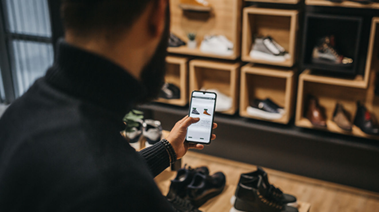 Person in shoe store holding phone with shoes on screen.