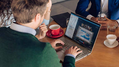 Three colleagues seated in a coffee shop attend a meeting on a secure 5G laptop.
