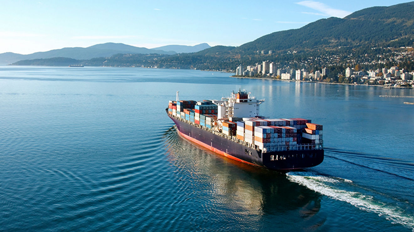Big ship with cargo containers off the coast of a city with mountains in the distance