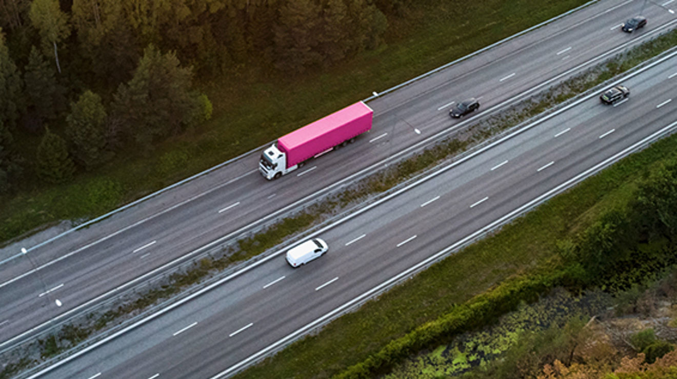 Overhead view of a highway with a white van and big rig with magenta and white colors 