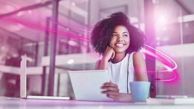 A happy business professional in an office looks up from their laptop.
