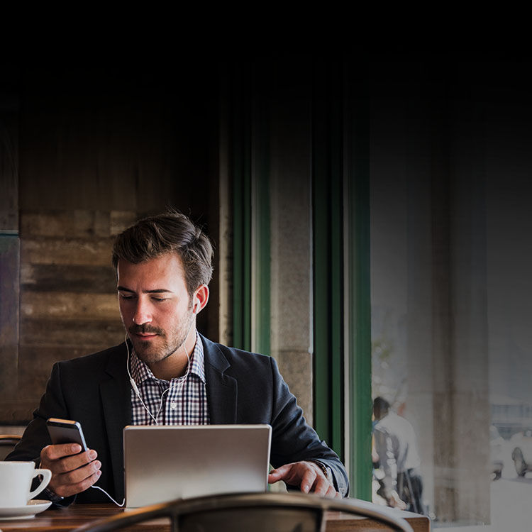 Man looking at his smartphone and laptop while sitting outside at a café.