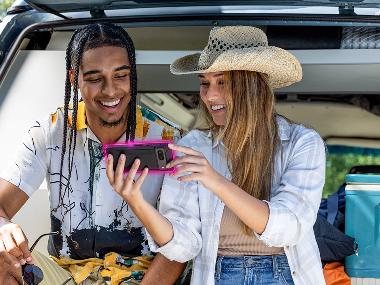 Two friends in the back of a vehicle smile at something they see on their phone.
